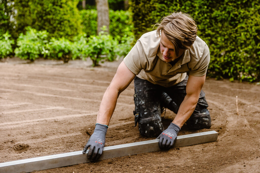 Ein Mitarbeiter von Verspeek Rollrasen bereitet den Untergrund vor und ebnet den Boden, um anschließend Rollrasen zu verlegen.