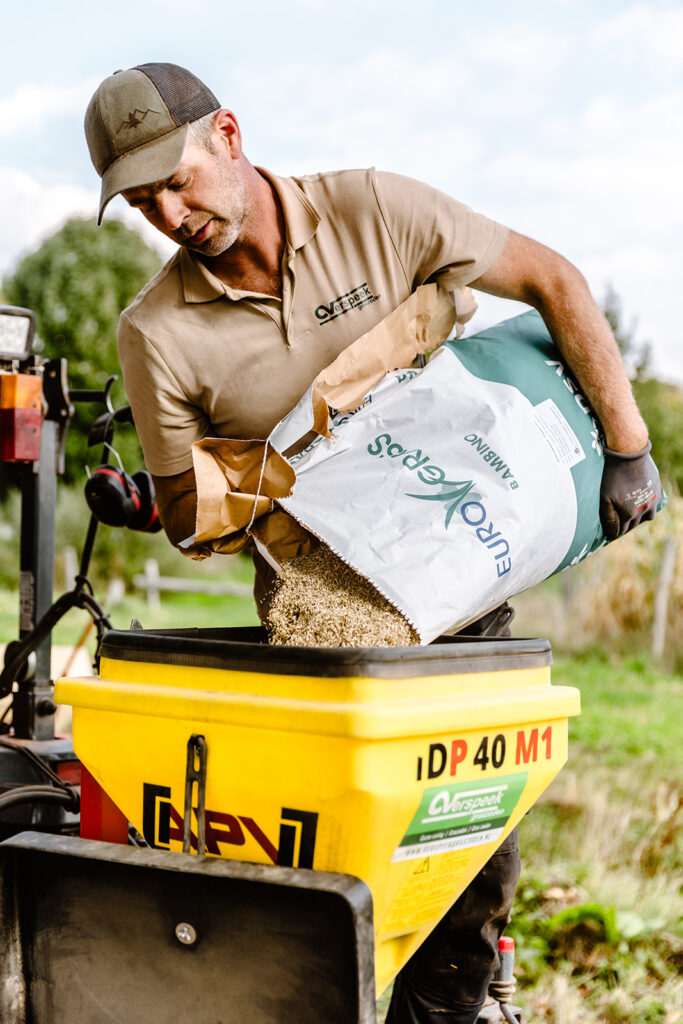 Ein Mitarbeiter von Verspeek Rollrasen füllt das Rasensaatgut sorgfältig in eine Rasensämaschine.