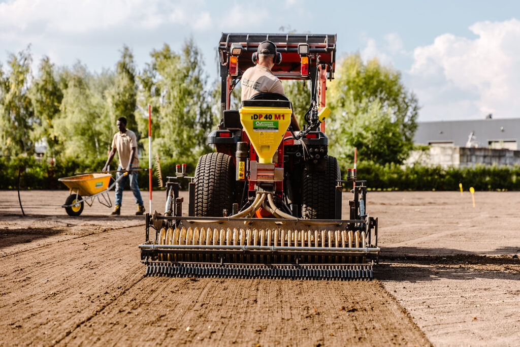 Traktor mit pneumatischer Sämaschine bei der Aussaat von Rasensamen auf einer großflächigen Gartenanlage. Die sorgfältige Bodenbearbeitung sorgt für gleichmäßiges Wachstum und eine dichte Grasnarbe.